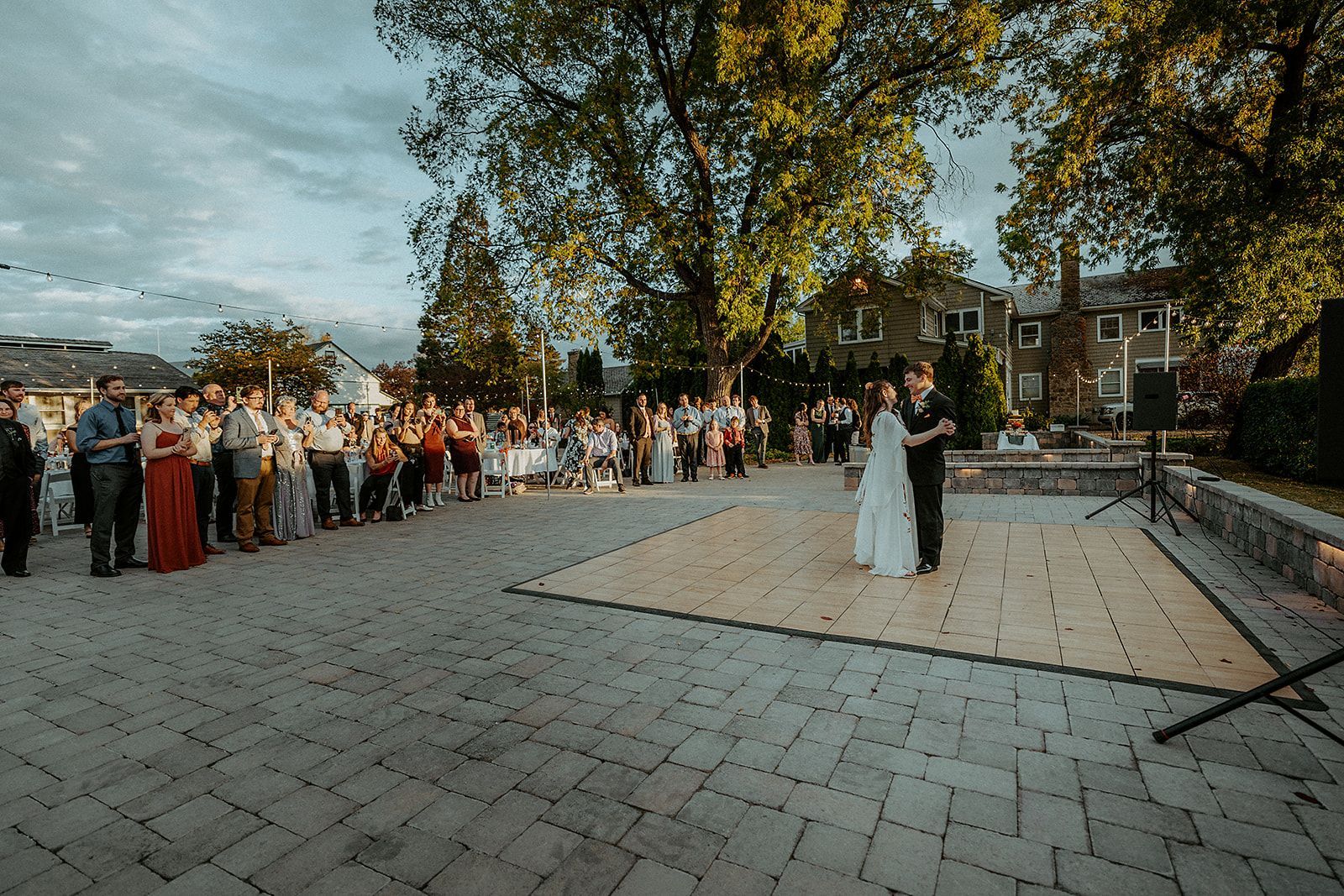 A bride and groom are dancing on a wooden dance floor in front of a crowd of people.