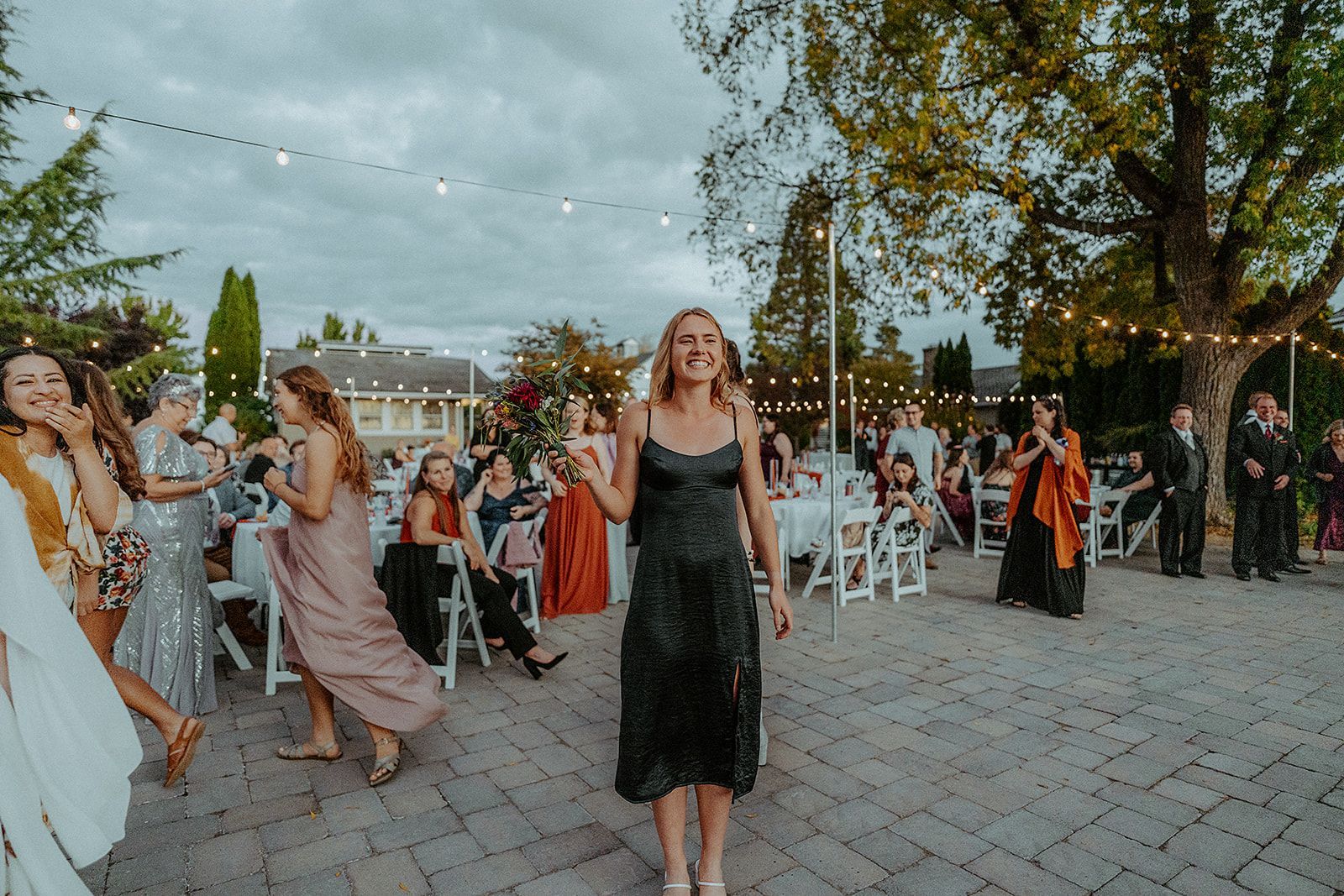 A woman in a black dress is holding the bouquet from a wedding at the wedding reception.
