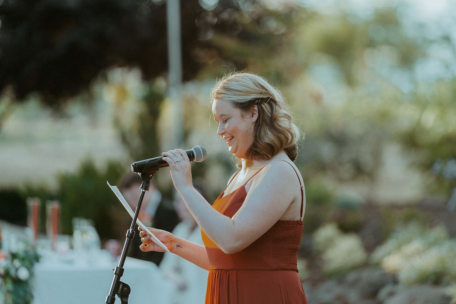 A woman in a red dress is giving a speech at a wedding.