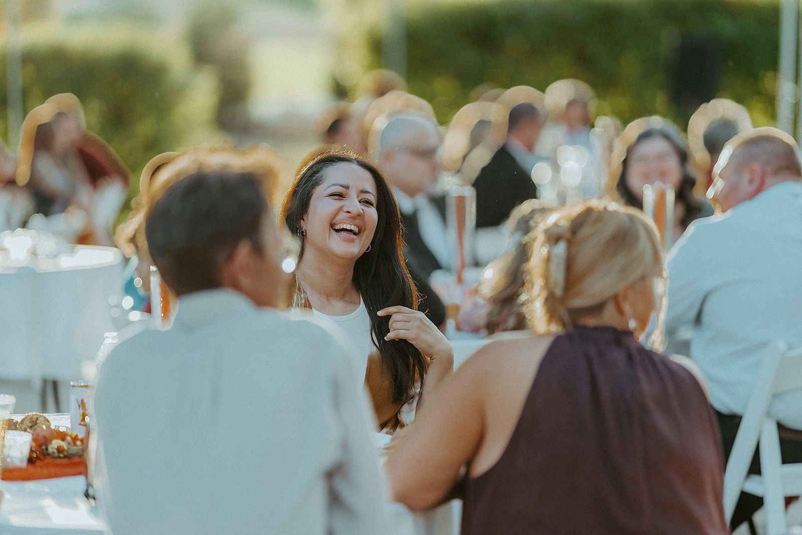 A group of people are sitting at tables at a wedding reception laughing.