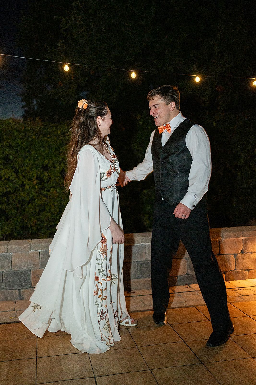 A bride and groom are dancing on a patio at their wedding reception.