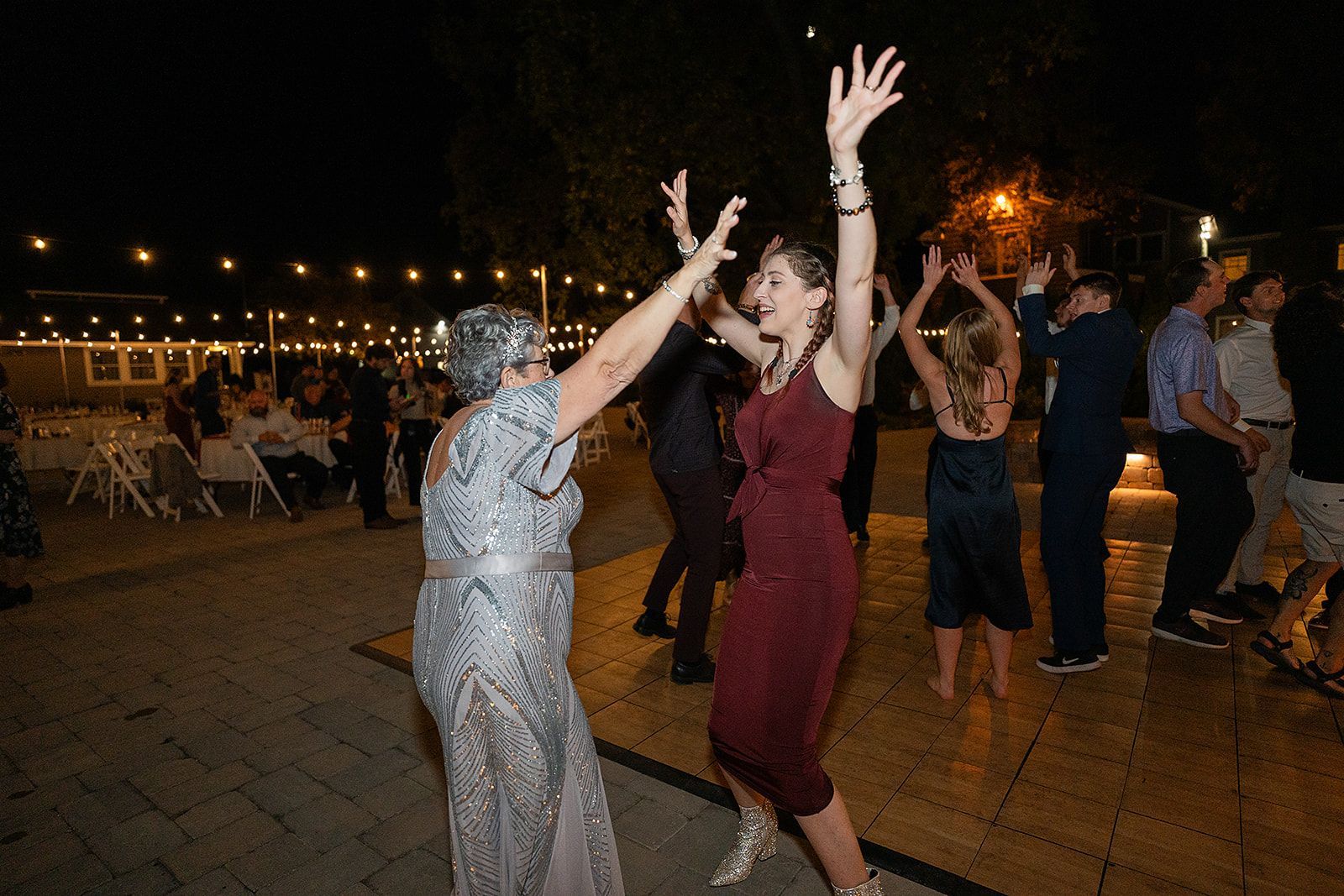 Two women are dancing at a wedding reception with their arms in the air.