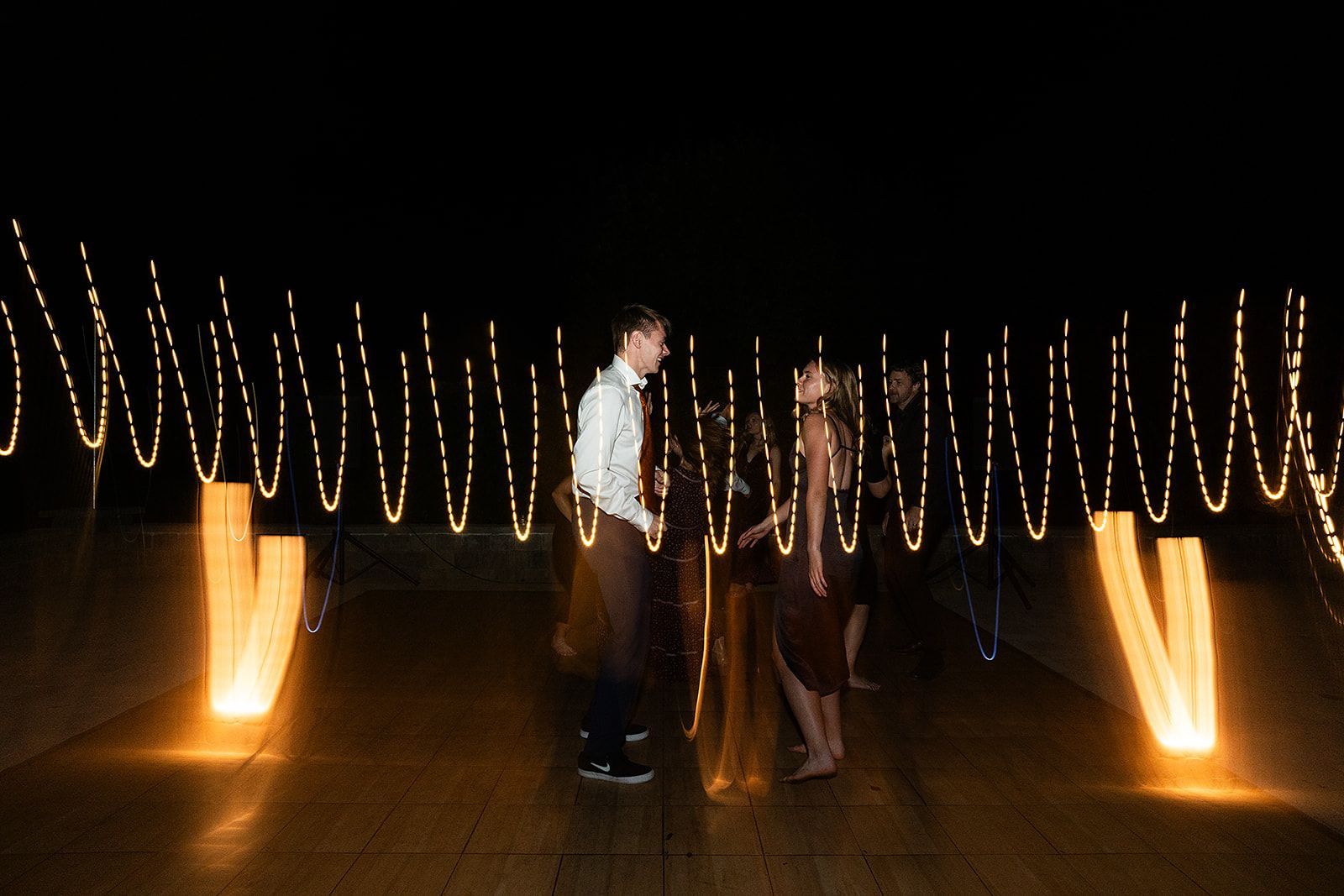 A man and a woman are dancing in front of a row of lights.