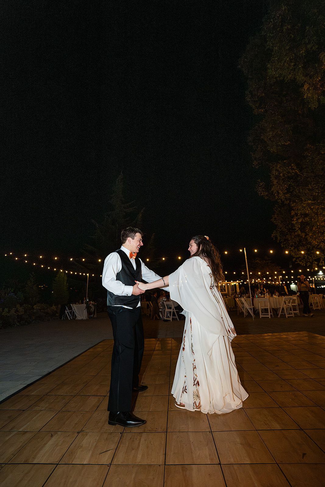 A bride and groom are dancing on a wooden dance floor at night.