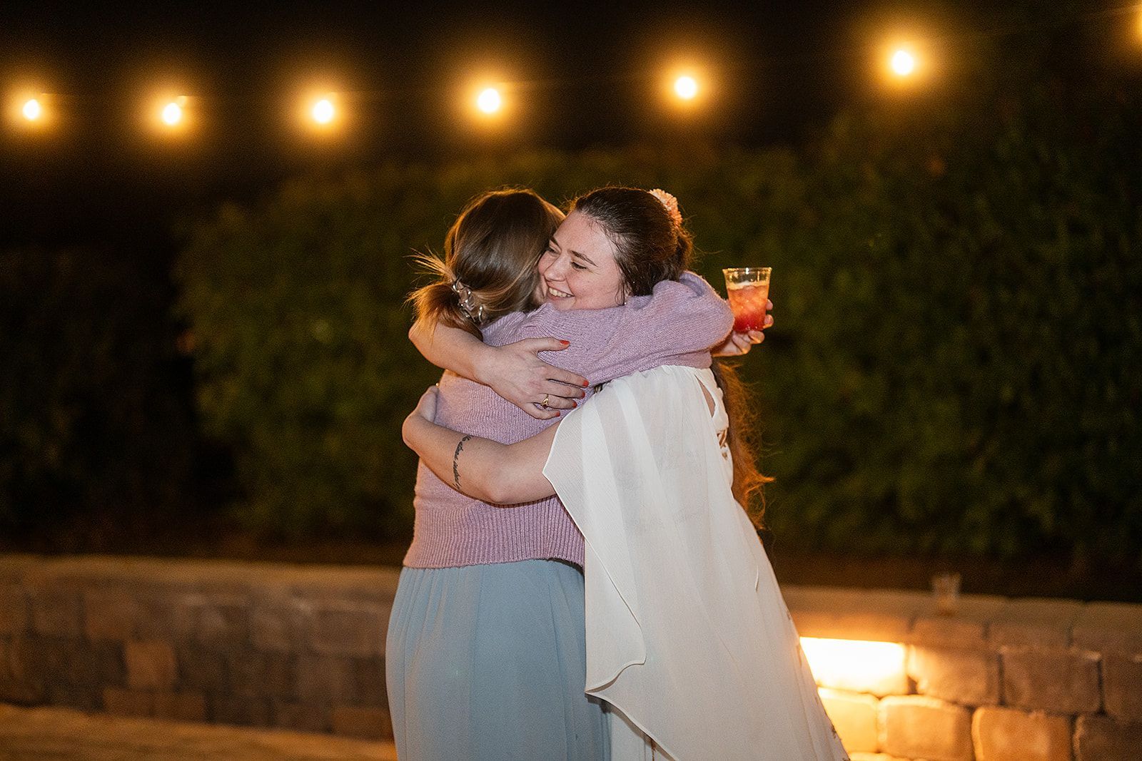 Two women are hugging each other in front of a string of lights.