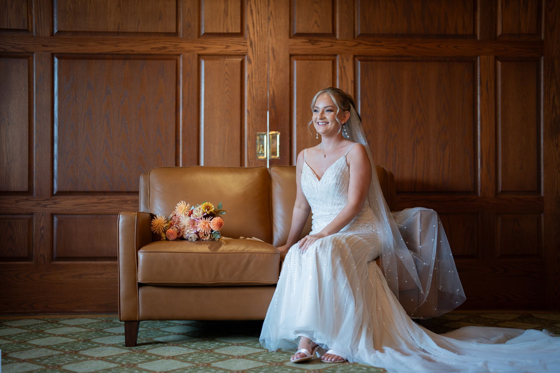 A bride in a wedding dress is sitting on a couch holding a bouquet of flowers.