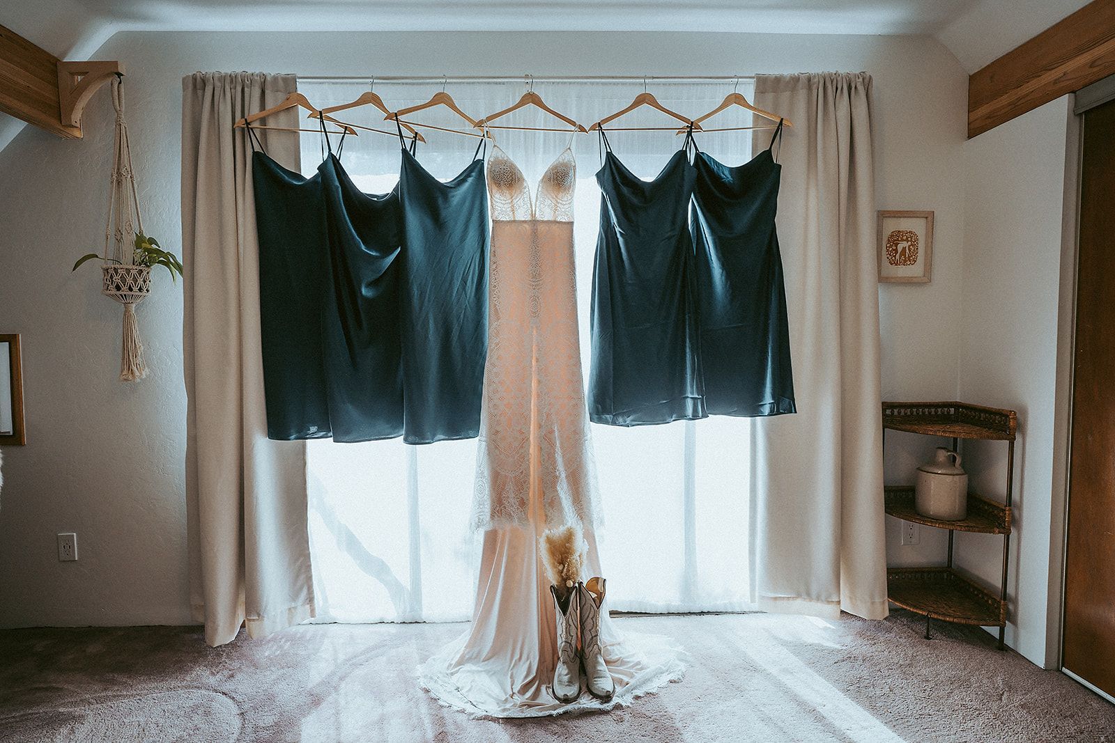 A wedding dress and bridesmaid dresses are hanging in a room.