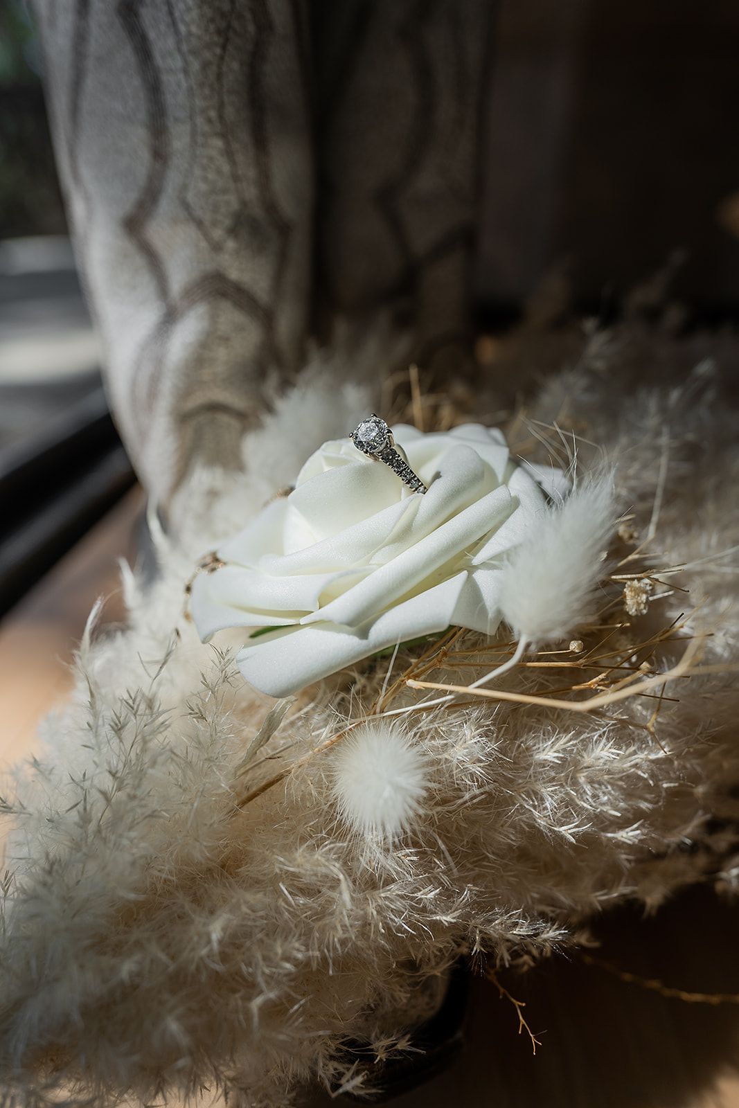 A wedding ring is sitting on top of a white rose.