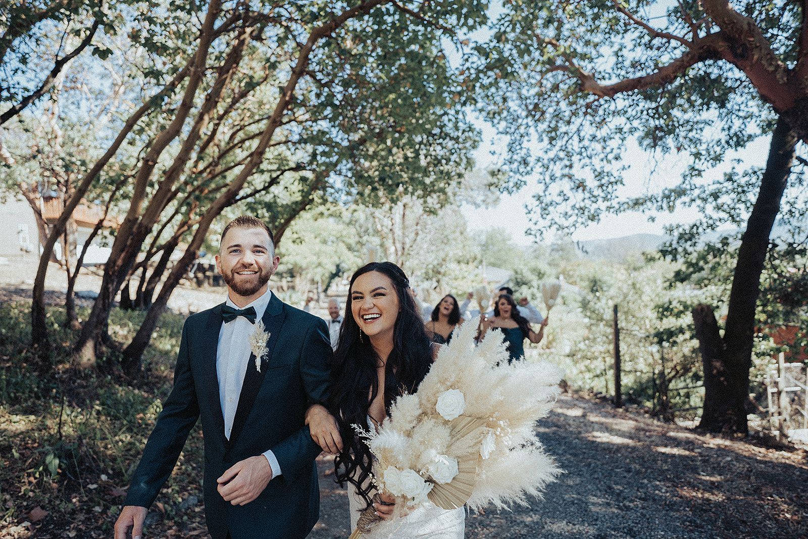 A bride and groom are walking down a dirt road with their wedding party.