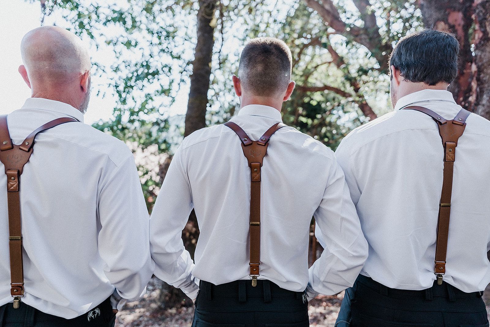 Three men wearing white shirts and brown suspenders are standing next to each other.