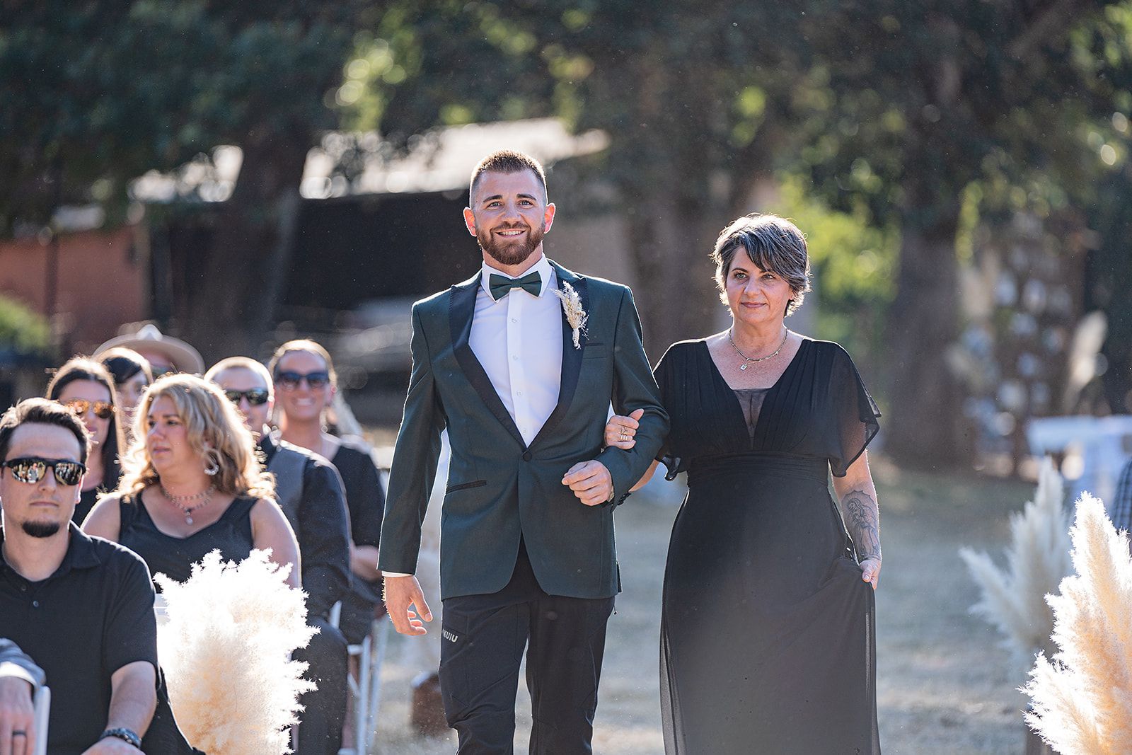 A groom and his mother are walking down the aisle at a wedding.