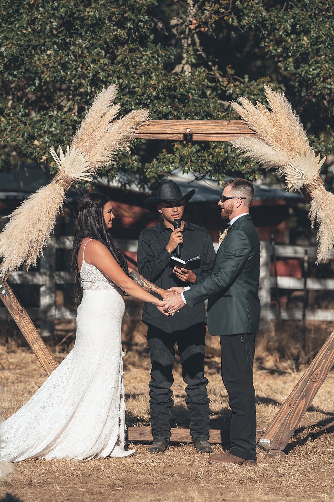 A bride and groom are holding hands during their wedding ceremony under a wooden arch.