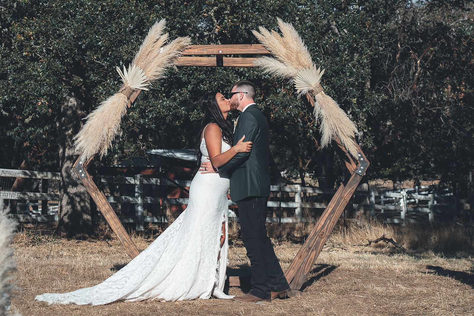 A bride and groom are kissing under a wooden arch at their wedding.