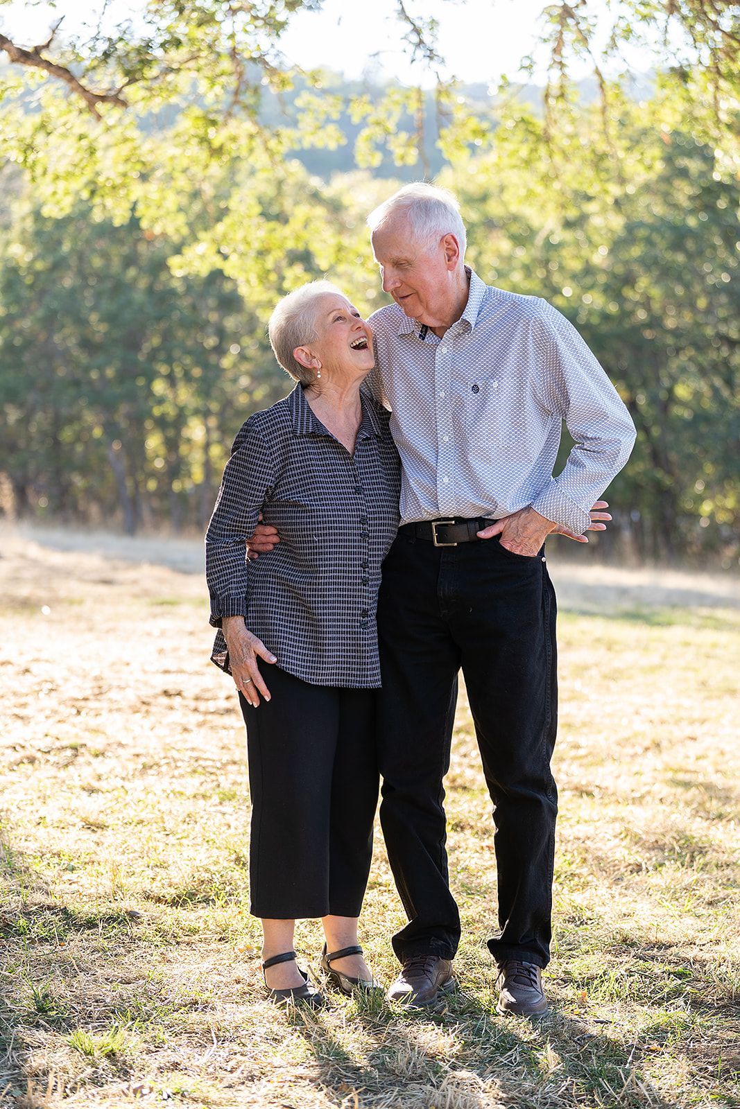 An elderly couple standing next to each other in a field.