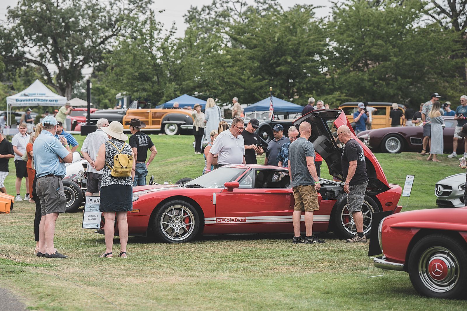 A group of people are standing around a red car at a car show.