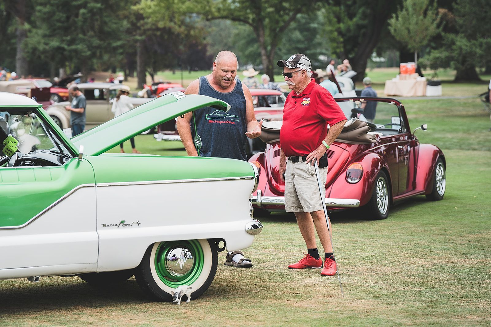 Two men are standing next to a green and white car at a car show.