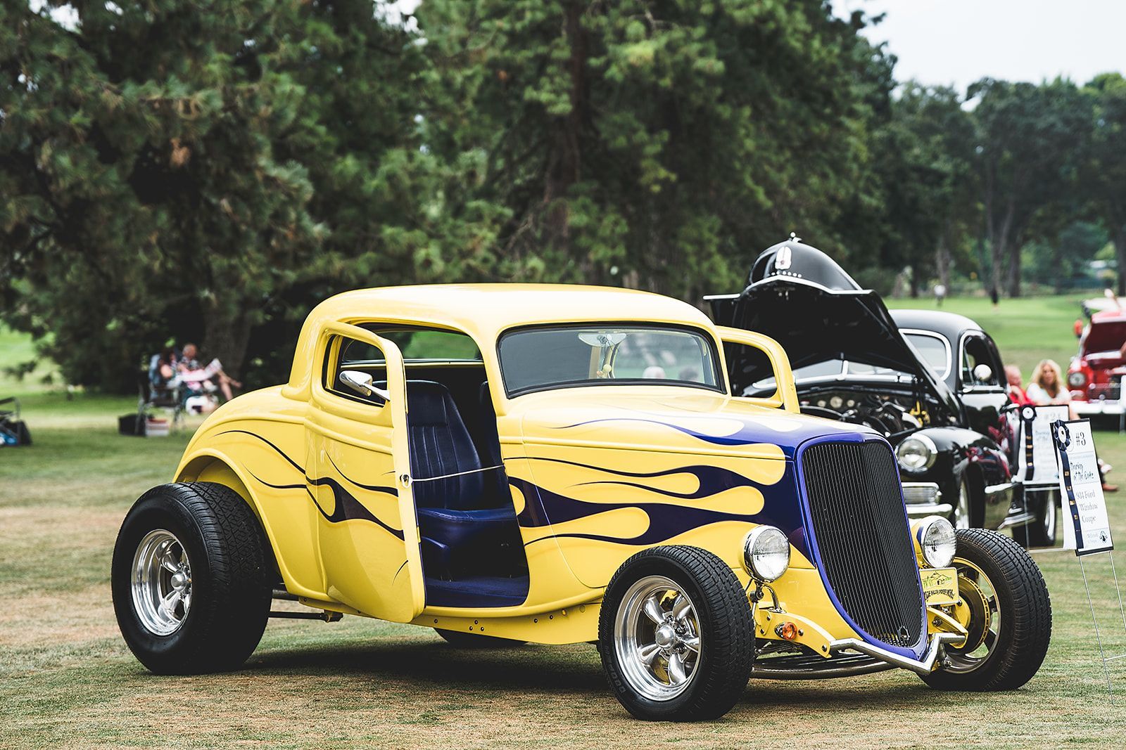 A yellow and blue hot rod is parked in a grassy field.
