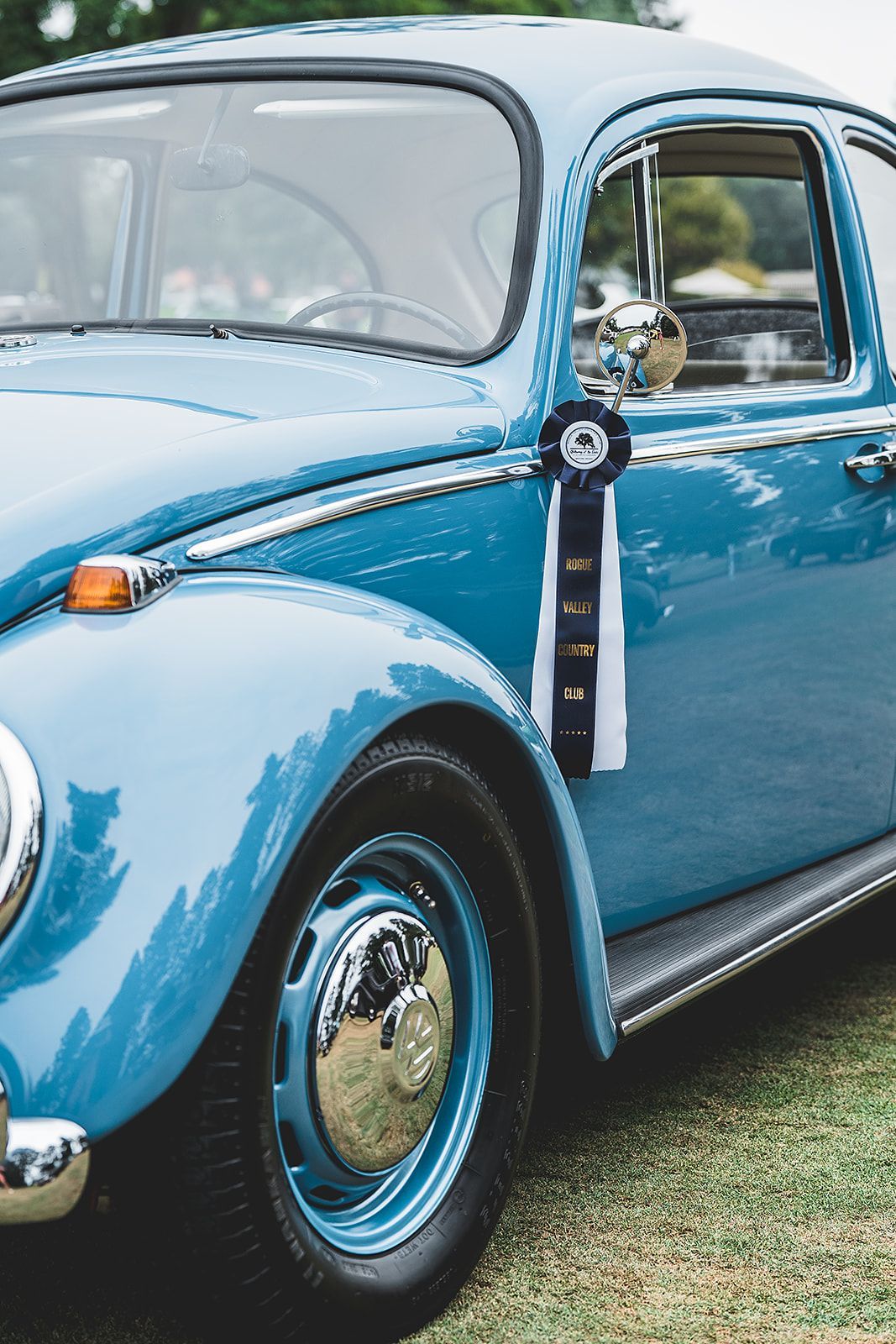 A blue car with a ribbon on the door is parked on the grass.