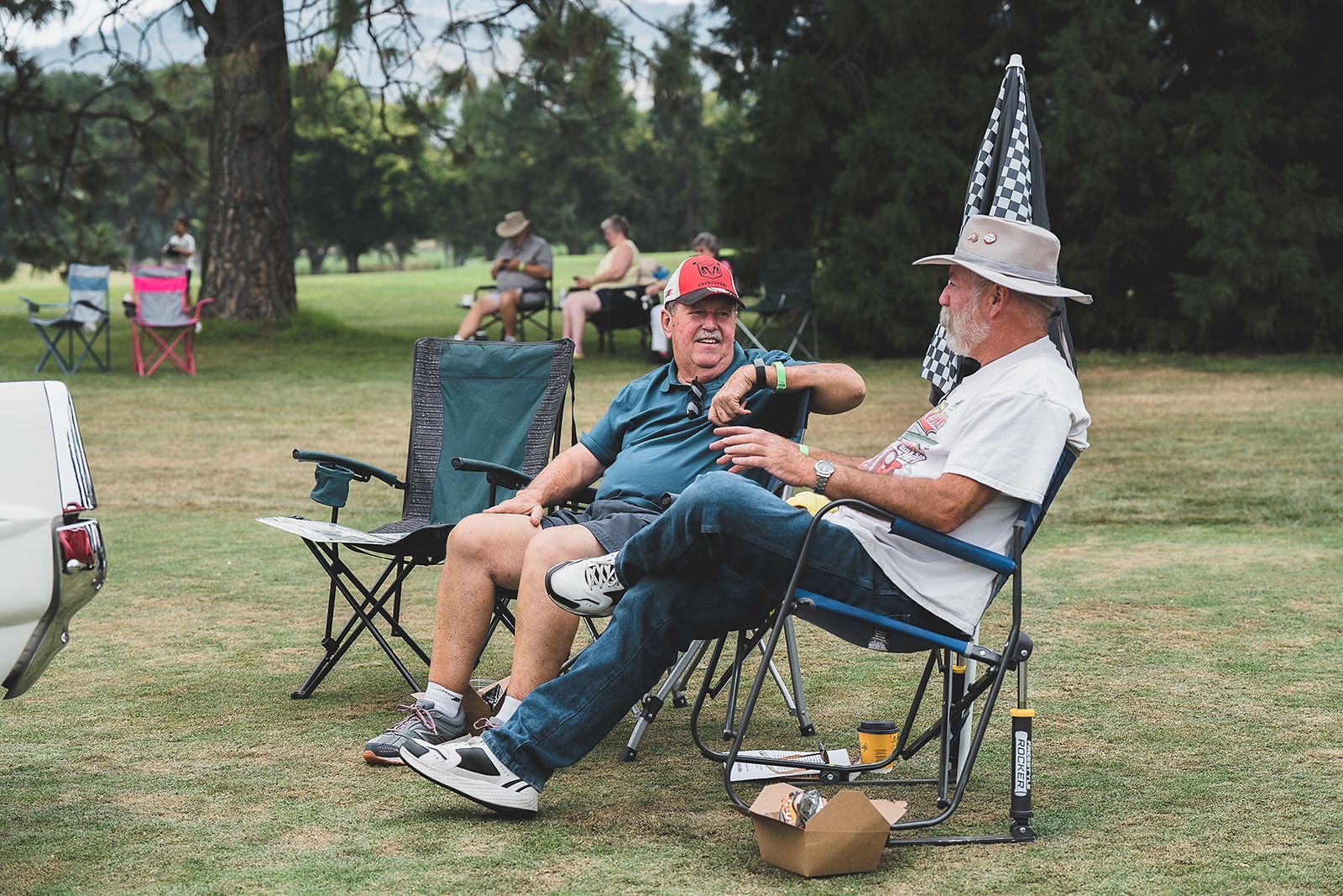 Two men are sitting in chairs in a park talking to each other.