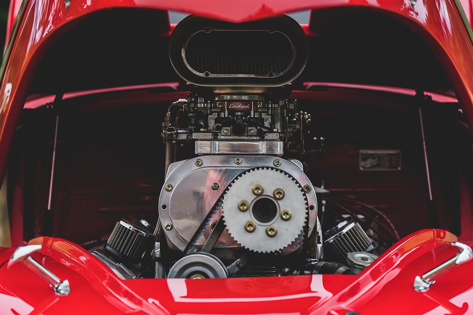 The engine of a red car is visible under the hood.