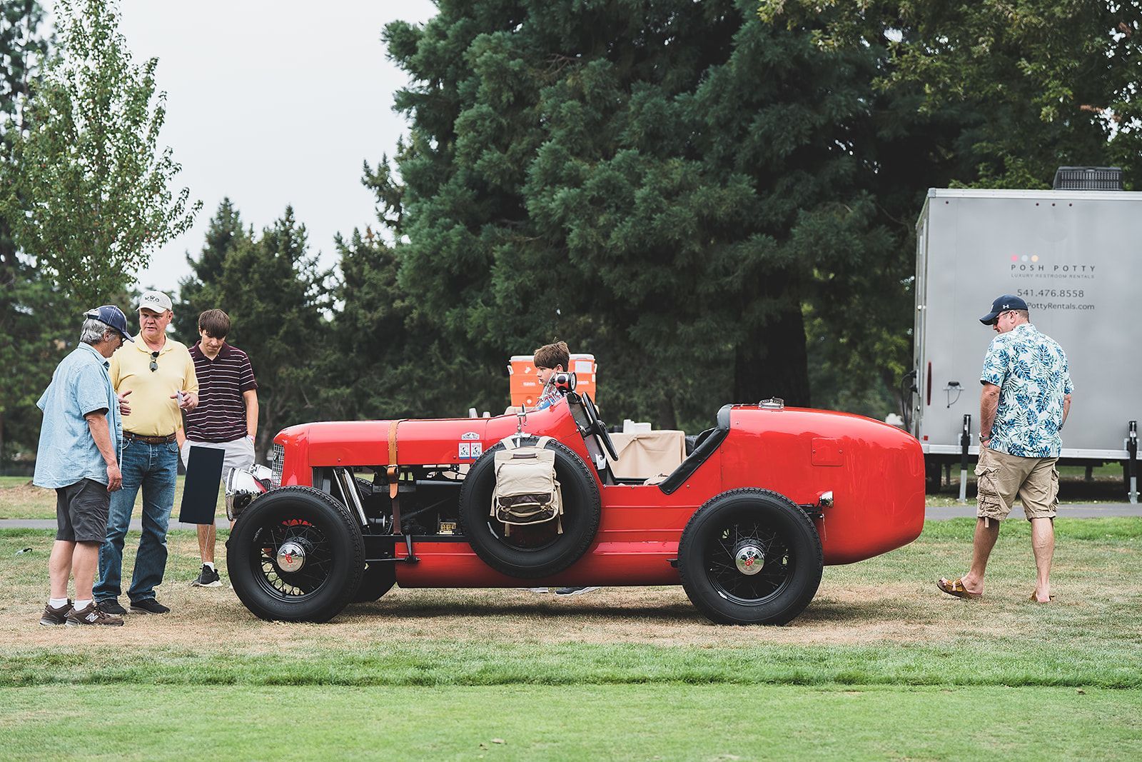A group of people are standing around a red car.