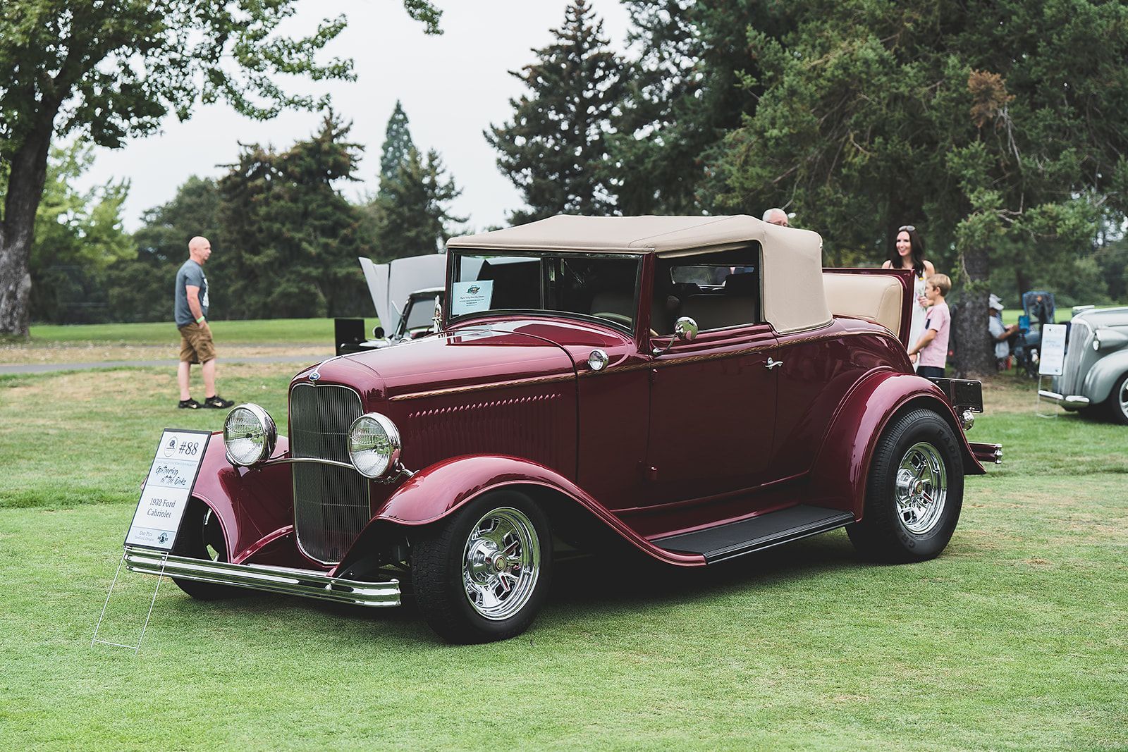 An old red car is parked in the grass at a car show.