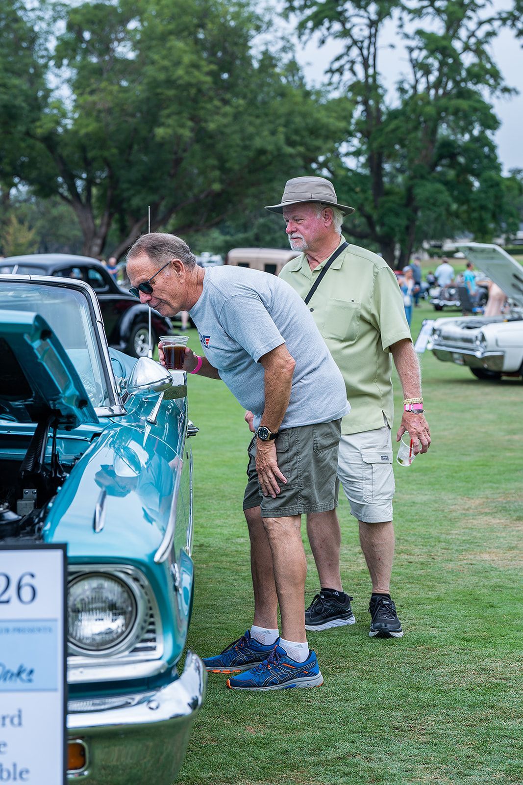 Two men are looking at a blue car at a car show.