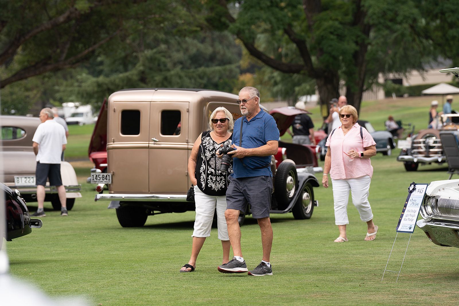 A man and a woman are standing next to each other in a field at a car show.