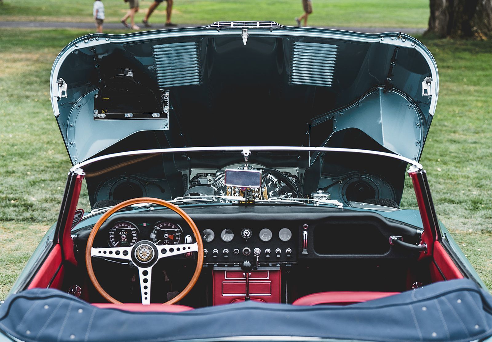 A convertible car with the hood open is parked in a grassy field.