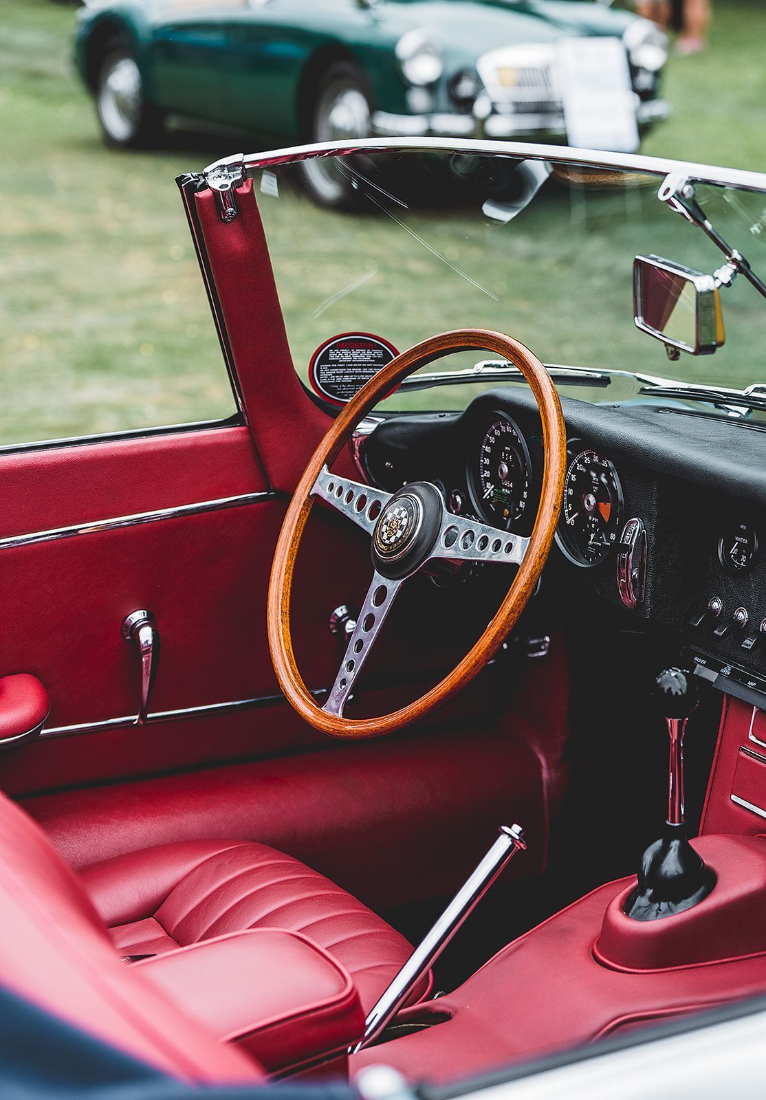 The interior of an old car with red seats and a wooden steering wheel.