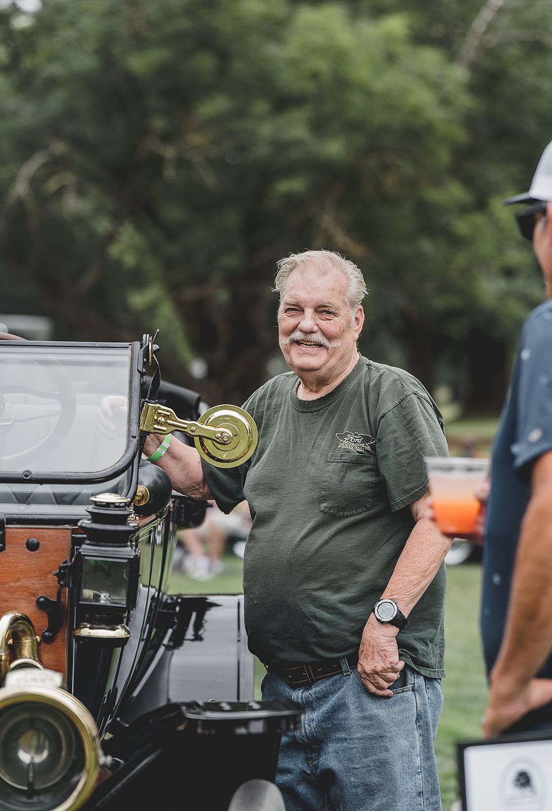 A man in a green shirt is standing next to an old car.