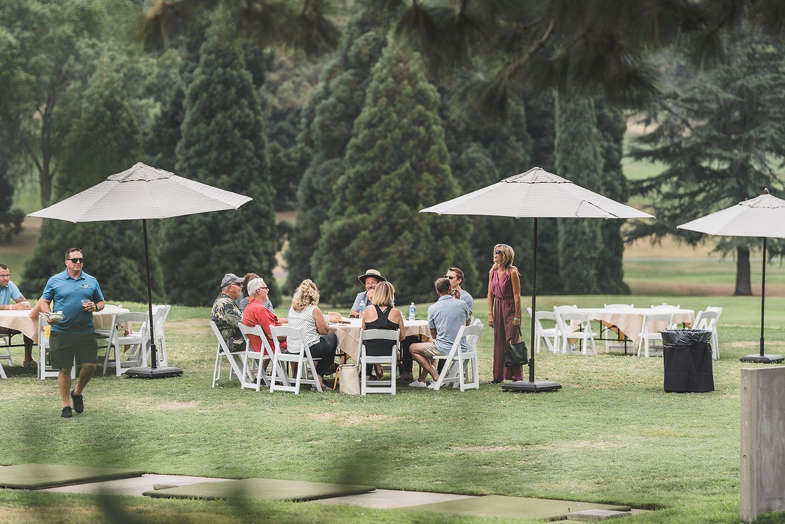 A group of people are sitting at tables under umbrellas in a park.