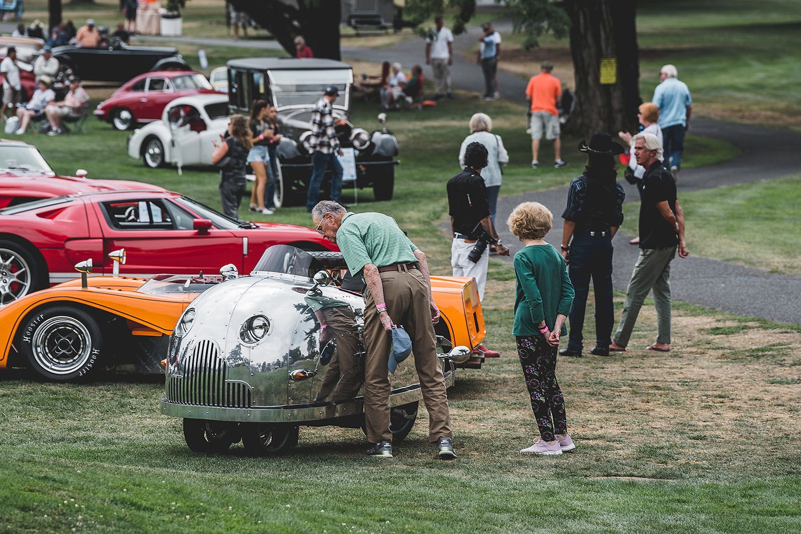 A group of people are standing around a row of cars at a car show.