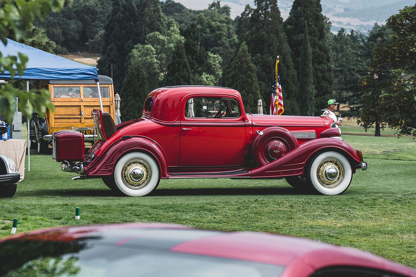 A red car is parked in a grassy field at a car show.