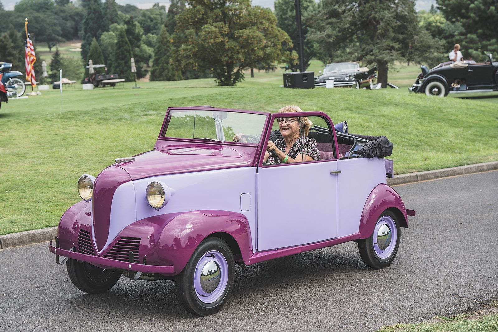 A woman is driving a purple car down a road.