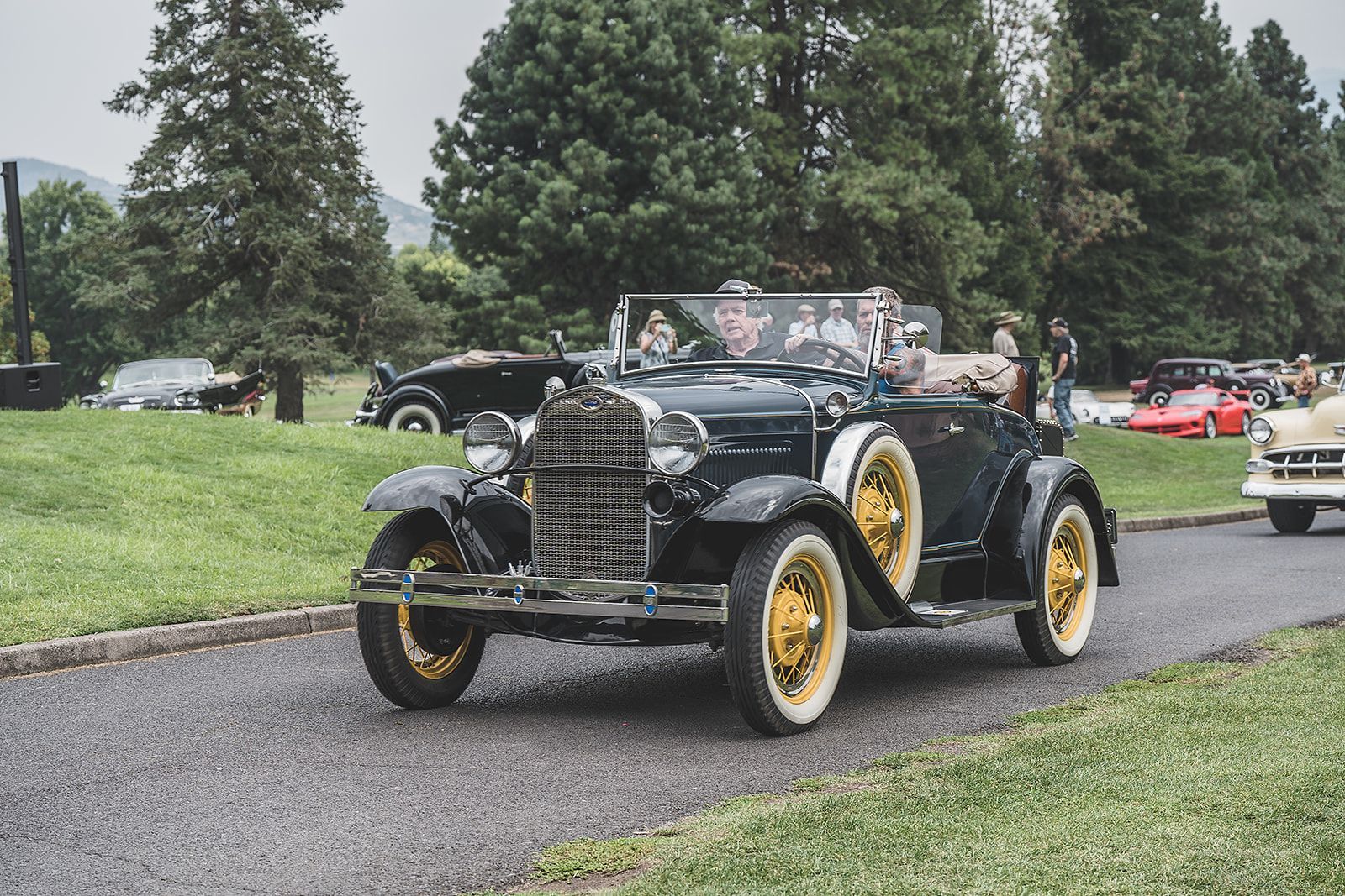 A couple of old cars are driving down a road.