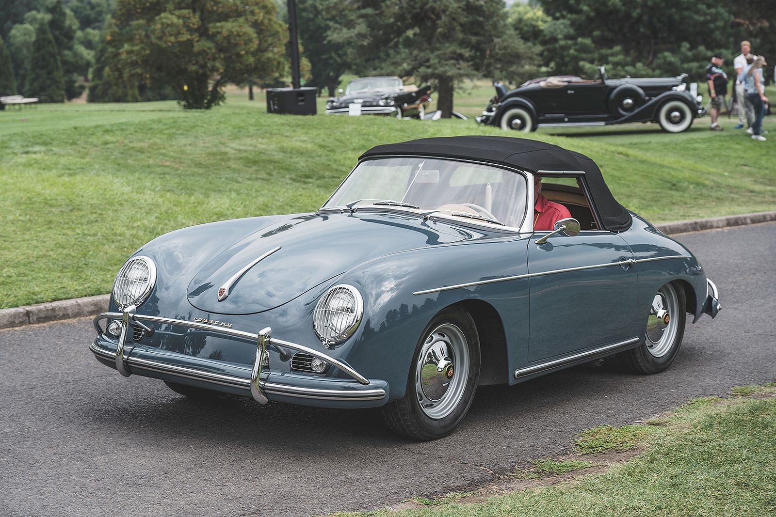 A blue porsche speedster convertible is driving down a road.