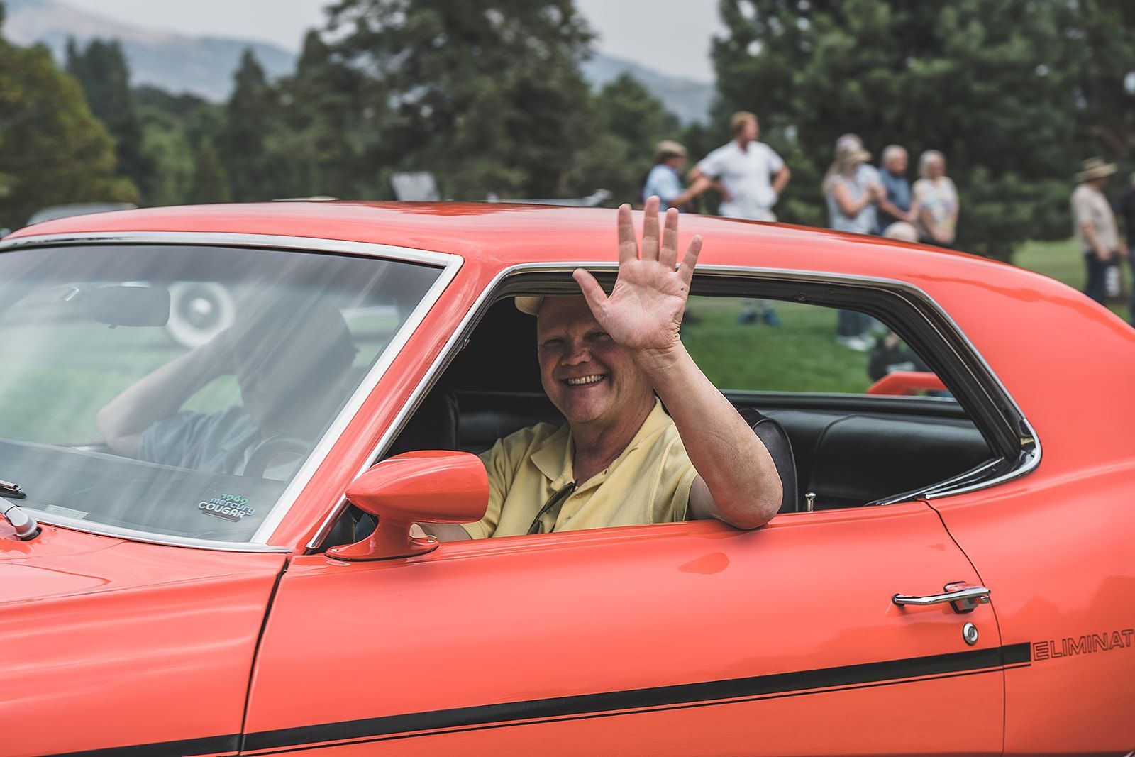 A man is waving from the window of an orange car.