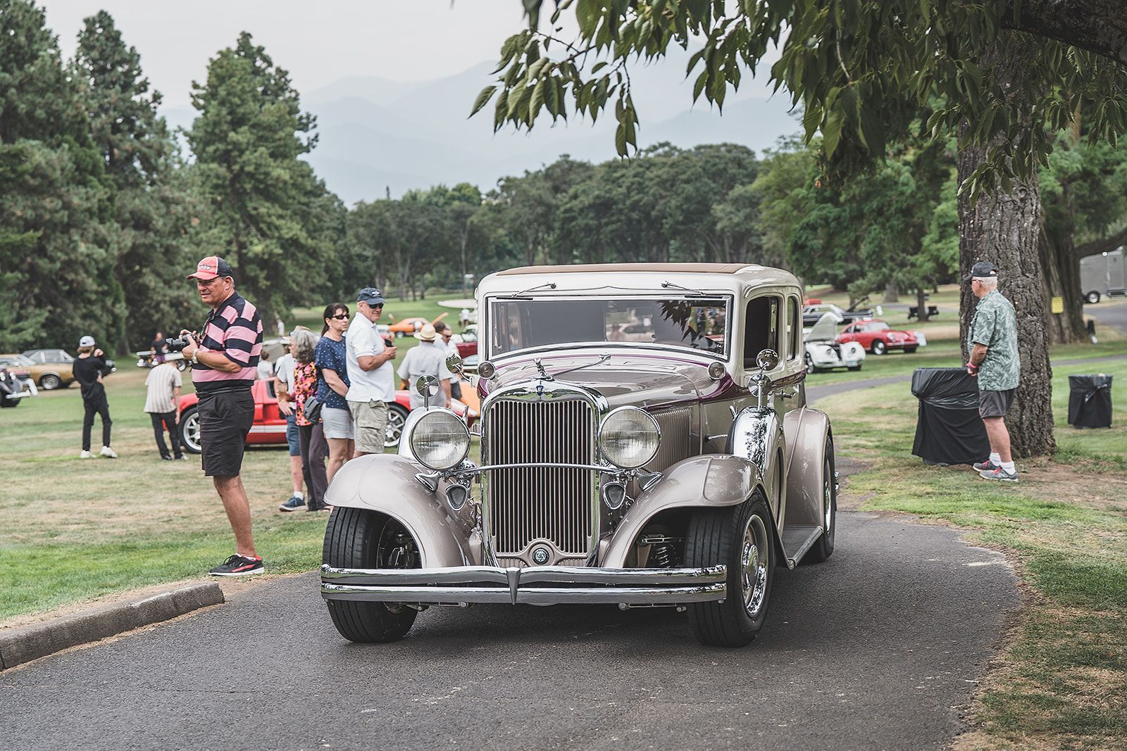 An old car is parked on the side of the road in a park.