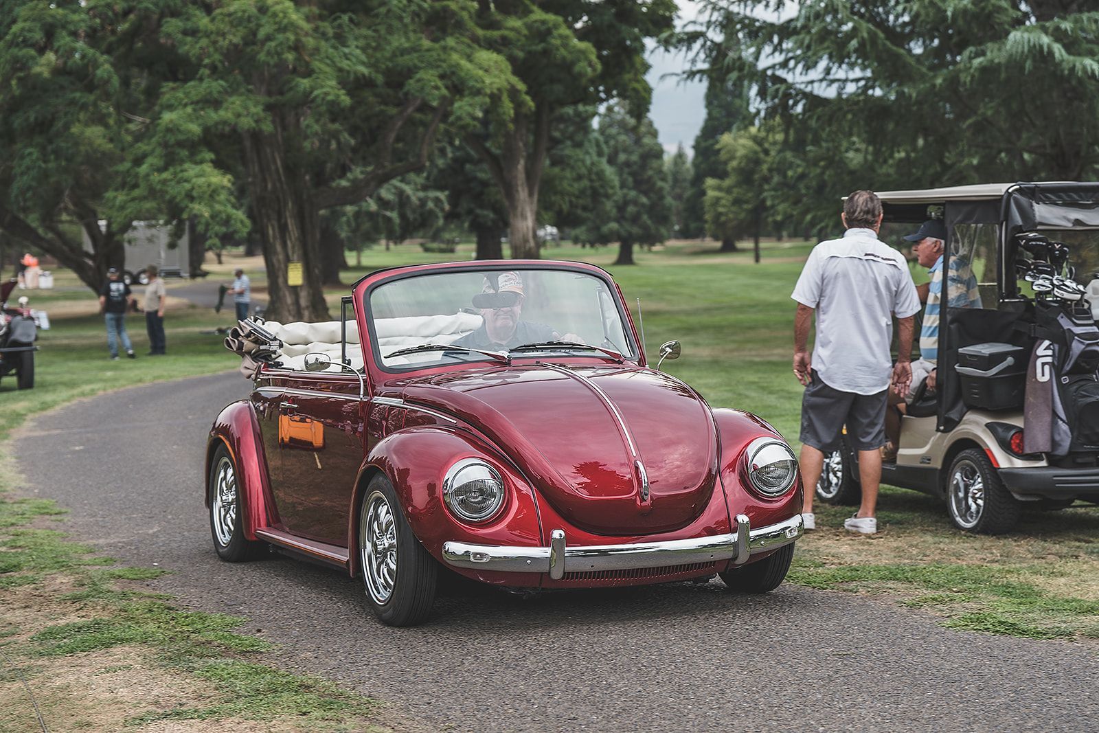 A red beetle convertible is parked in a park next to a golf cart.