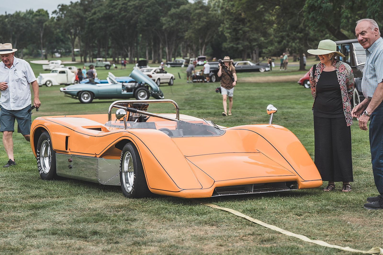 A group of people are standing around an orange sports car at a car show.