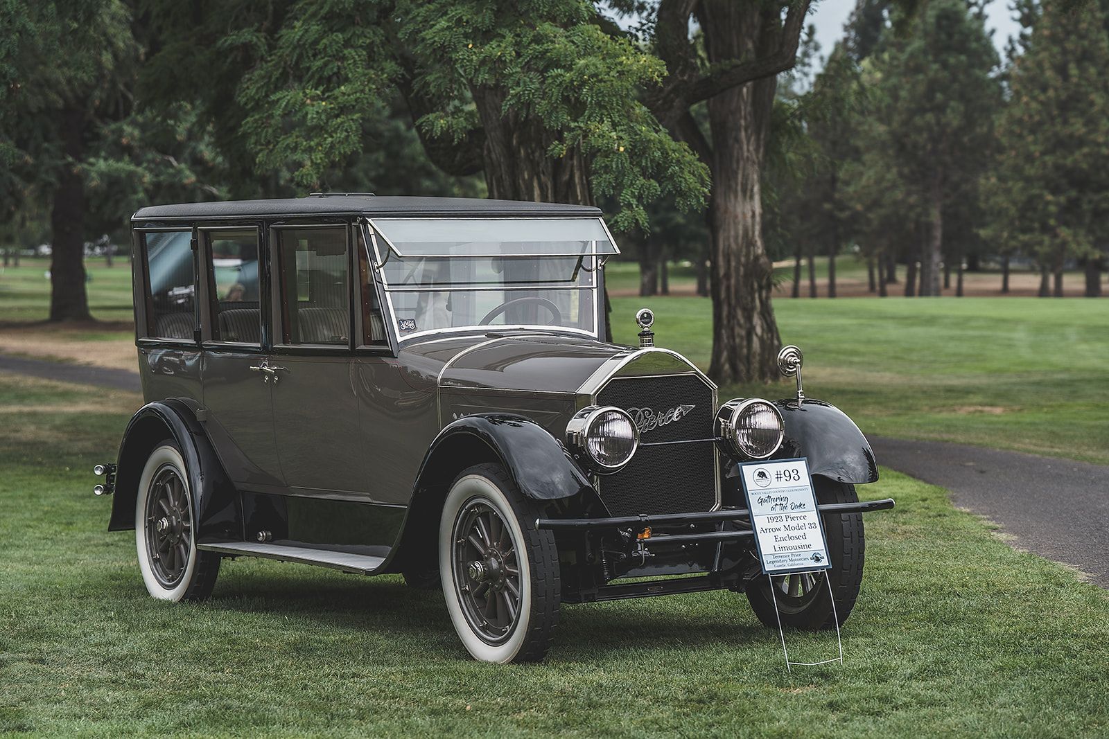 An old car is parked in the grass in a park.
