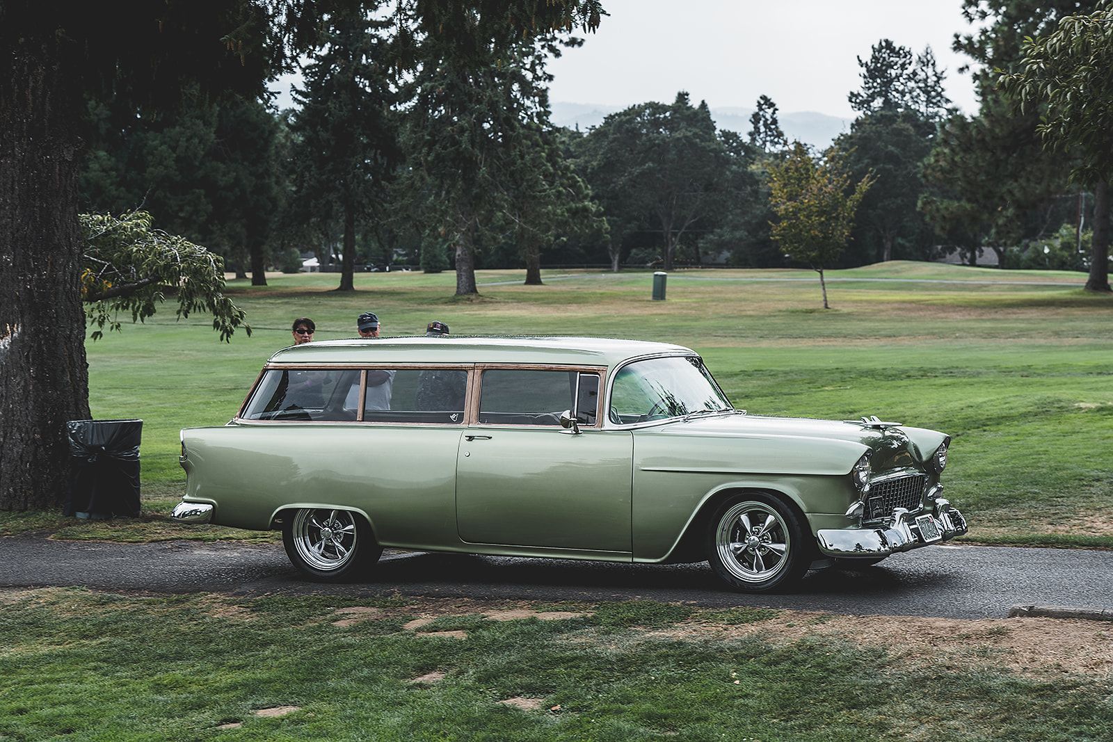 An old green station wagon is parked in a park.
