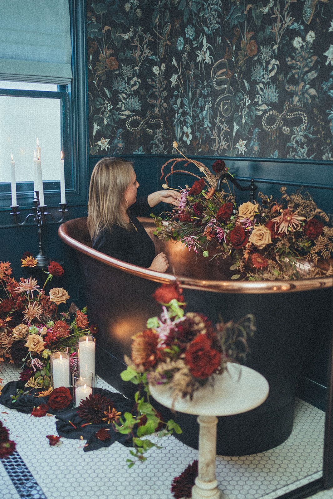 A woman is sitting in a bathtub surrounded by flowers and candles.