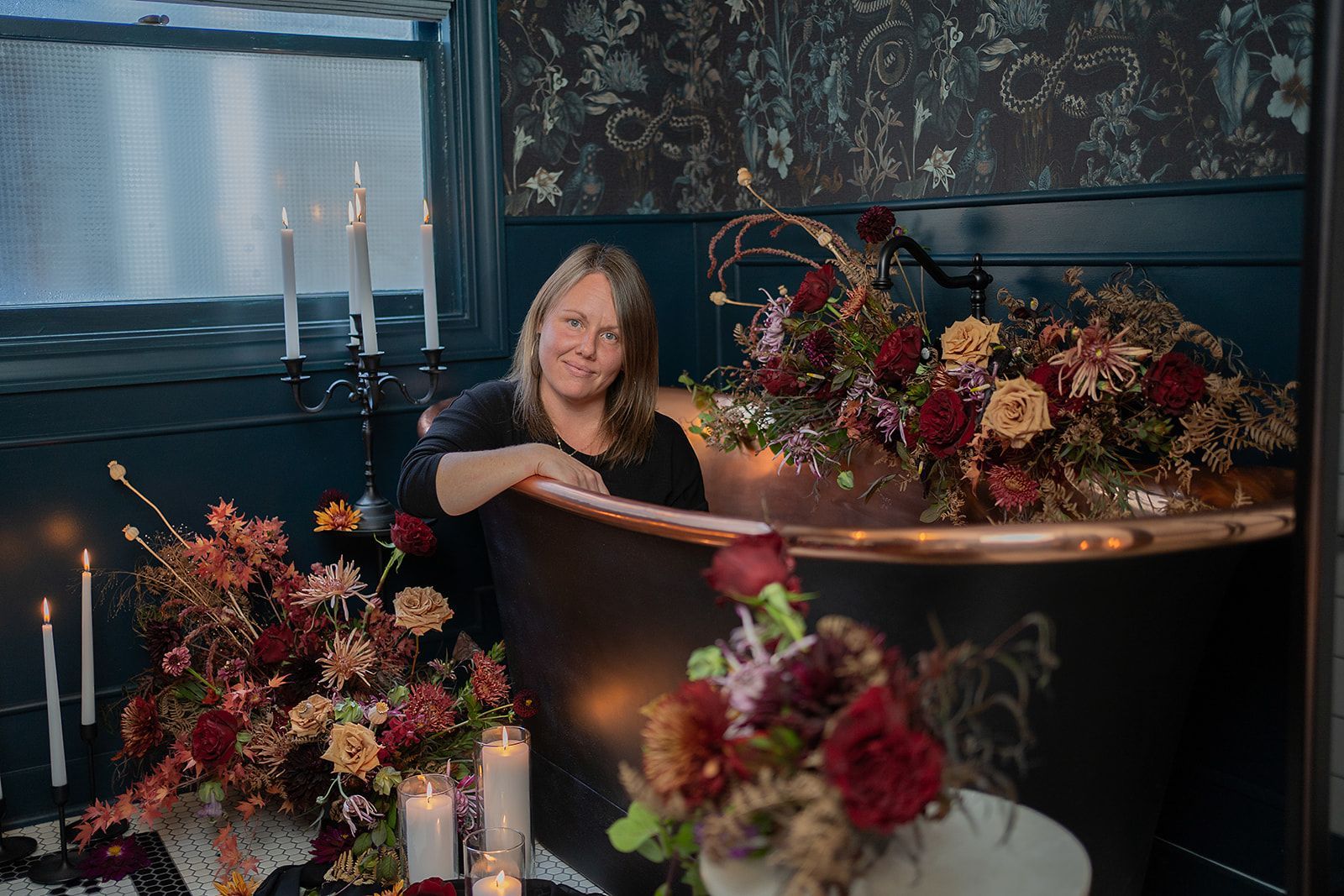 A woman is sitting in a bathtub surrounded by flowers and candles.