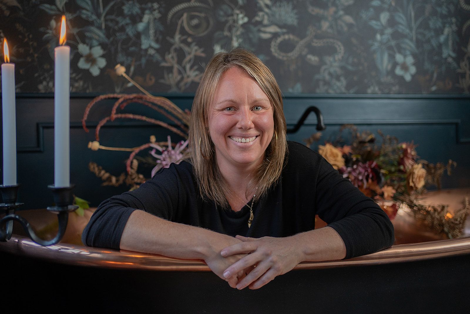 A woman is leaning on the edge of a bathtub with candles in the background.