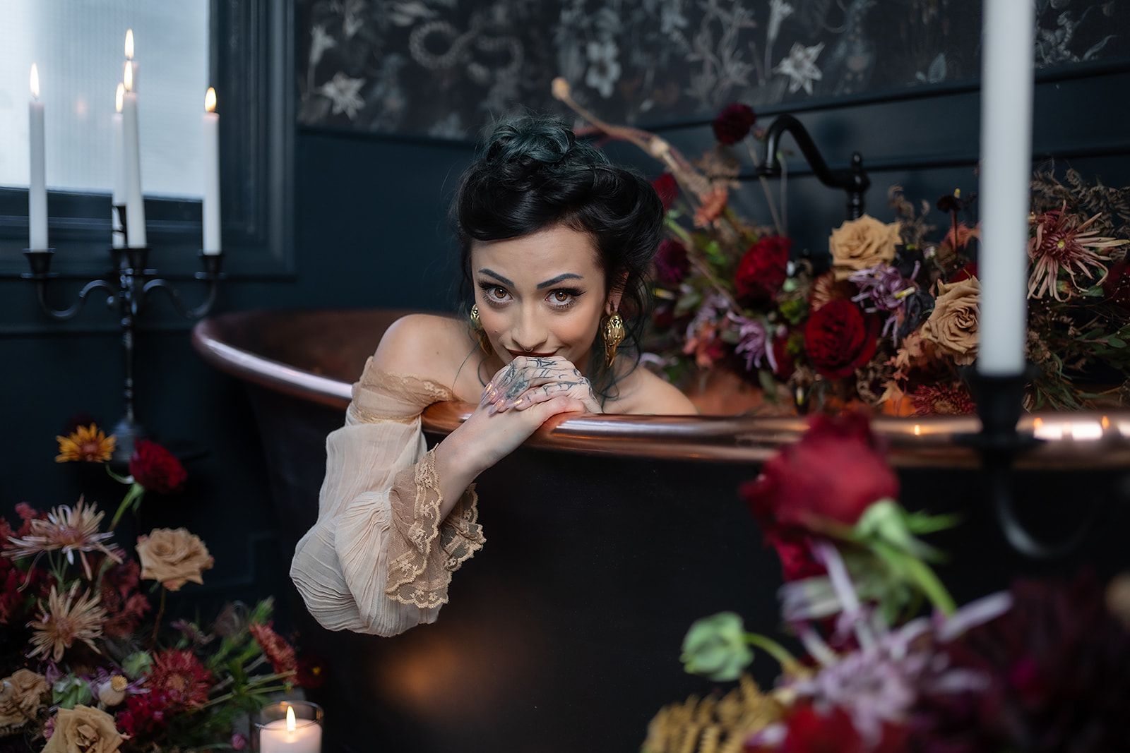 A woman is laying in a bathtub surrounded by candles and flowers.
