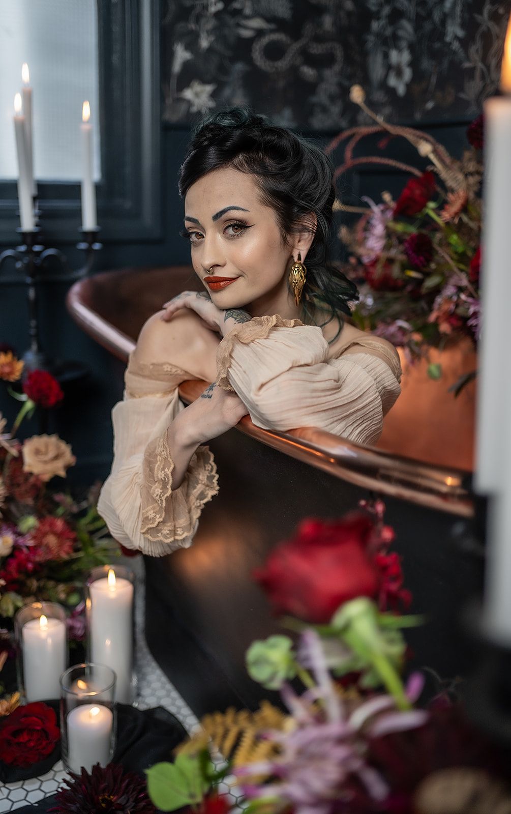 A woman is sitting in a bathtub surrounded by candles and flowers.