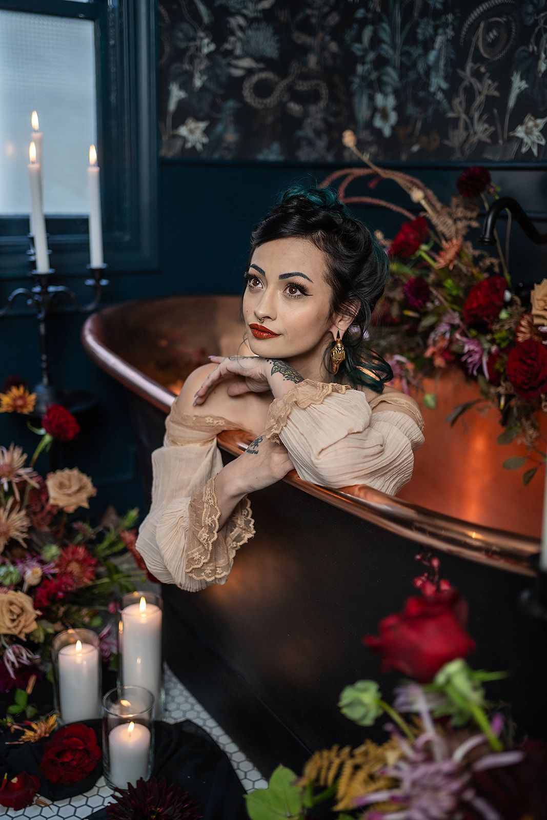 A woman is sitting in a bathtub surrounded by candles and flowers.