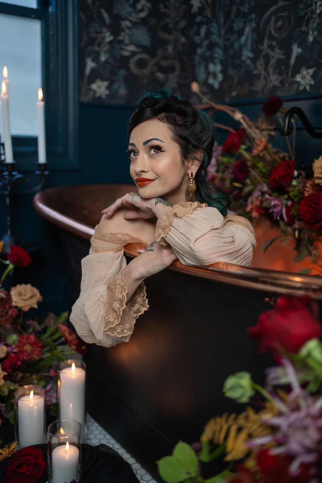 A woman is sitting in a bathtub surrounded by candles and flowers.